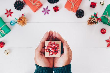 Top view of hand holding christmas gift with snowflakes and Pine cones on wooden white background.の写真素材
