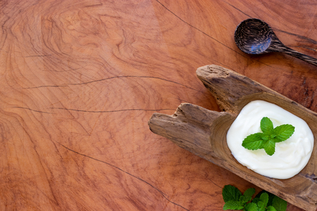 Top view of yogurt in a wooden bowl and mint  with  spoon on wooden table. Health food concept.の写真素材