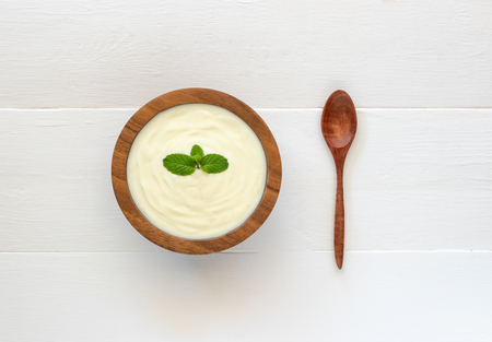 Top view of yogurt in a wooden bowl and mint with  spoon on white wooden table. Health food concept.の写真素材
