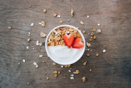 Top view of yogurt in a wooden bowl with granola,fresh strawberry on white wooden table. Health food concept.の写真素材