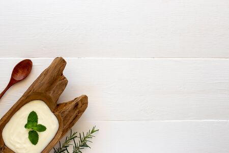 Top view of yogurt in a wooden bowl and mint with  spoon on white wooden table. Health food concept.の写真素材