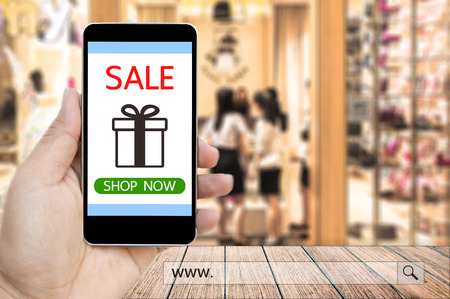 Hand holding smart phone with sale paynow on screen and www. search bar over blur people in the shopping mall background, business and financial concept.の写真素材