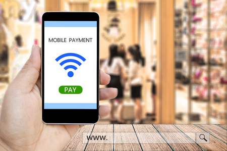 Hand holding smart phone with mobile payment and www. search bar over blur people in the shopping mall background, business and financial concept.の写真素材