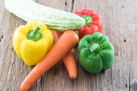 Group of fresh vegetables three sweet Red, Yellow, Green Peppers,  momordica,carrot  on wooden backgroundの写真素材