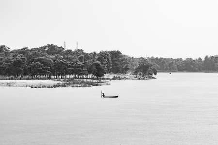Black and white scenic view of river bank, trees, mountain and fishing boatの写真素材