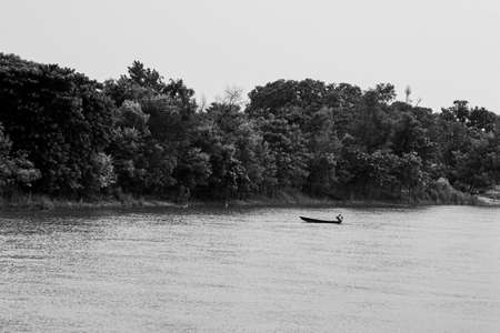 Black and white scenic view of river bank, trees, mountain and fishing boatの写真素材