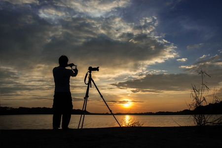 Silhouette of photographer with his equipment during sunset hand check compositionの写真素材