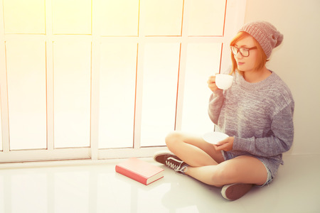 Beautiful young woman drinking coffee in the bedroom near the window at the morning