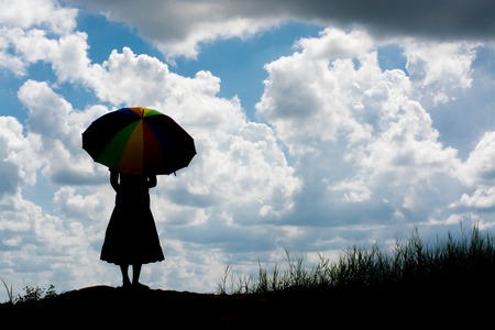 woman holding umbrella standing alone at the field during beautiful sunsetの写真素材
