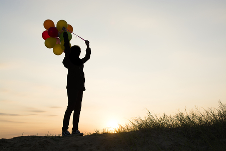 silhouette of Young  woman holding colorful of balloons with sunsetの写真素材