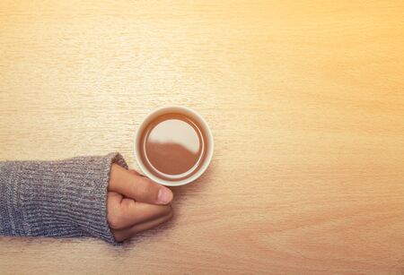 one of young woman hands holding a cup of hot drink on the wooden table