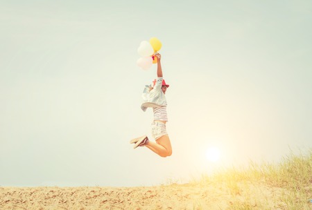 Beautiful Girl jumping with balloons on the beachの写真素材