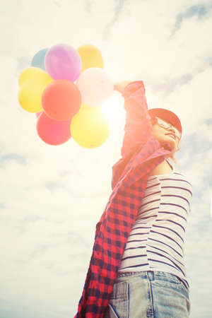 Hand of a teenage girl holding colorful balloons in the sunshine of summerの写真素材