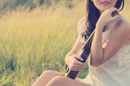 Beautiful Woman sitting  hand hugs violin in the meadowの写真素材