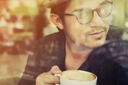 Young man drinking coffee inside cafe with sunriseの写真素材