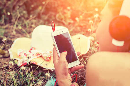 Close-up woman hands using smartphone to listening music laying and enjoying music in flower fieldの写真素材