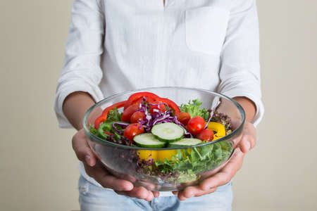 hands of beautiful woman holding big bowl of fresh veggie salad in the morningの写真素材