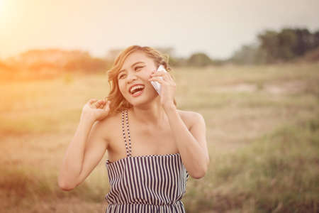 Beautiful sexy woman standing talking on phone in the grass field look so happyの写真素材