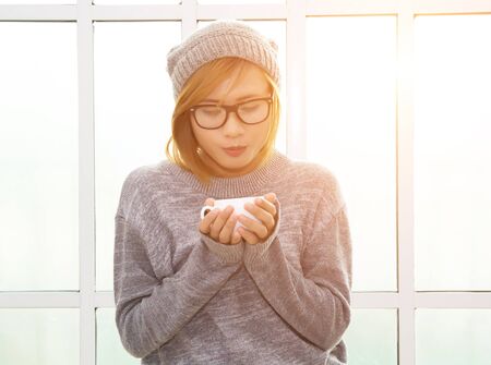 Young hipster woman holding a cup of coffee near window look so beautifulの写真素材