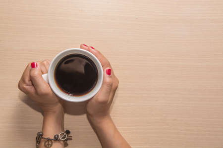 Woman's hands hold a cup of coffee on wooden table.の写真素材