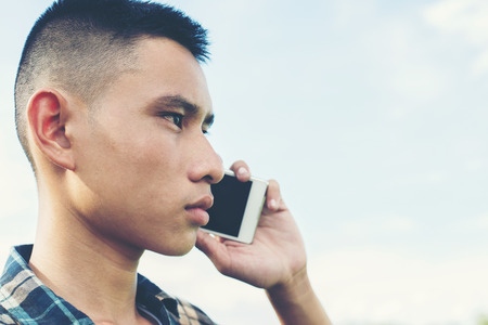 Young man talking on the phone and standing on the grass in the park.の写真素材