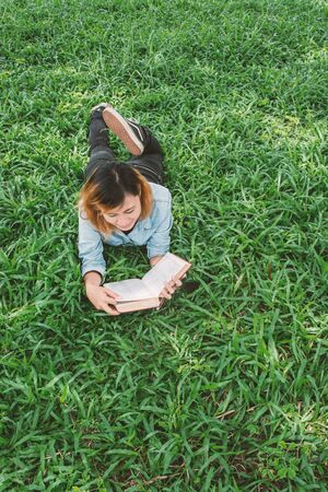 Young beautiful hipster woman reading book in the grass.の写真素材