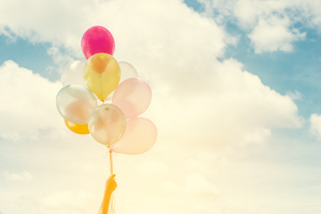 Woman lifestyle concept: woman hands holding a bunch of colored balloons with blue sky summer time...