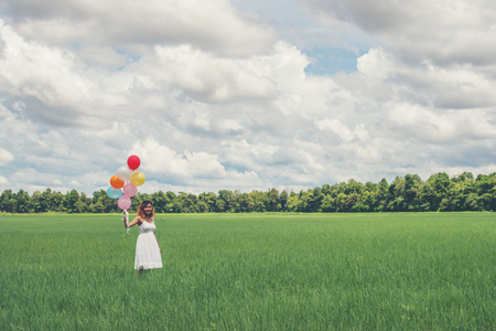Happy young beautiful woman with balloons in the grass field enjoy with fresh air.の写真素材
