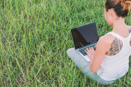 Young woman with laptop sitting on green grass at meadows.の写真素材