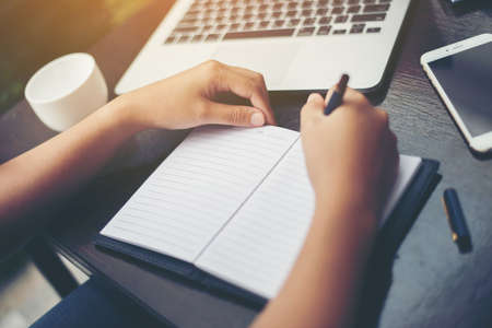 Close-up  of young beautiful woman hands writing and work with laptop computer.