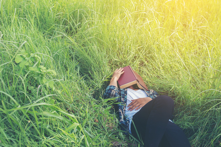 Young hipster man lying down on grassland napping tired after reading book with nature around.の写真素材