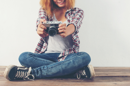 Young hipster photographer woman taking photo and look at camera sitting on wooden floor.の写真素材