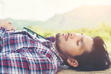 Happy young hipster lying on bench in the nature park.の写真素材