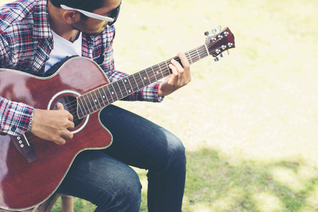 Portrait of young hipster man practiced guitar in the park,happy and enjoy playing guitar.の写真素材