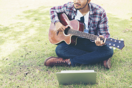 Young hipster man practiced guitar with laptop in the park,happy and enjoy playing guitar.の写真素材