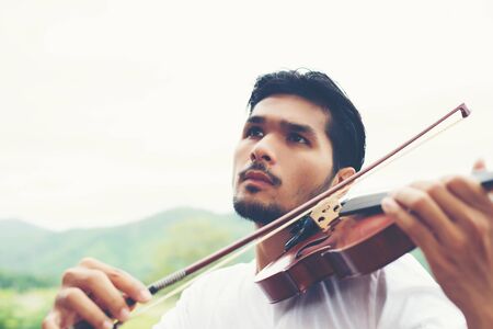 Young hipster musician man play violin in the nature outdoor lifestyle behind mountain.の写真素材