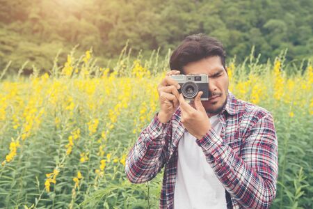 Young handsome hipster man photographing with retro camera with nature yellow flower field.の写真素材