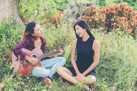 Young teenage looking at her female friend while playing guitar,Relaxing time enjoyment.の写真素材