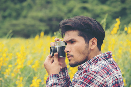 Young handsome hipster man photographing with retro camera with nature yellow flower field.の写真素材
