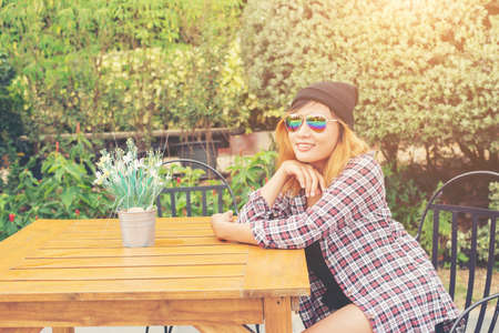 Outdoor portrait of young hipster woman sitting alone at old city cafe and waiting for her boyfriend wearing plaid outfit and  sunglasses.の写真素材