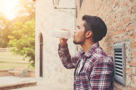 Young hipster bearded man with water bottle in plaid shirt in front of urban background.