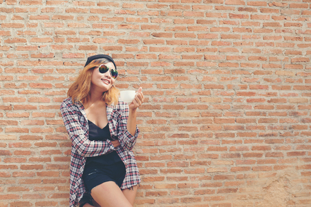Cheerful woman in the street drinking morning coffee against brick wall.の写真素材