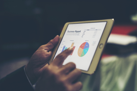 Business person hand holding financial statistics displayed on the tablet screen at office.の写真素材