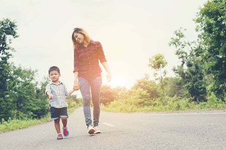 Happy mom holding hand with his son walking on the street.の写真素材