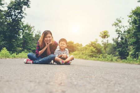 Mother and son sitting enjoy playing on the road and looking at the camera.の写真素材