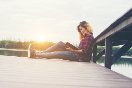 young beautiful hipster woman relaxing sitting on pier reading book.の写真素材