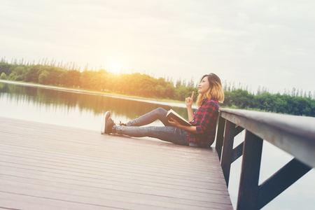 young beautiful hipster woman relaxing sitting on pier reading book.の写真素材
