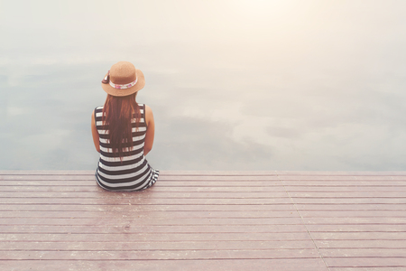 Back of young woman wearing hat sitting at the pier,relaxing enjoy with nature.の写真素材
