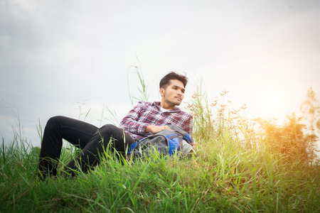 Young hipster man take a rest on the meadows after hiking, look away to find out another adventure.の写真素材