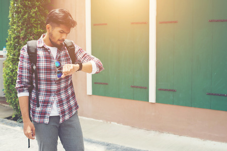 Young man looking at his hand-watch before go to travel with backpack on his shoulder.の写真素材